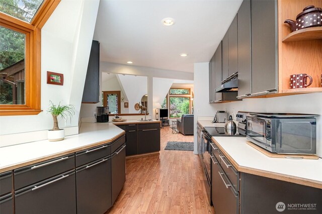 kitchen with electric range, black microwave, light countertops, light wood-style flooring, and under cabinet range hood