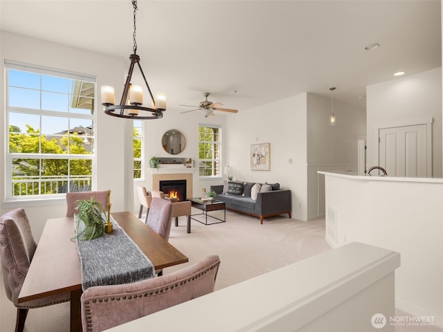 dining area featuring plenty of natural light, ceiling fan with notable chandelier, a warm lit fireplace, and light colored carpet