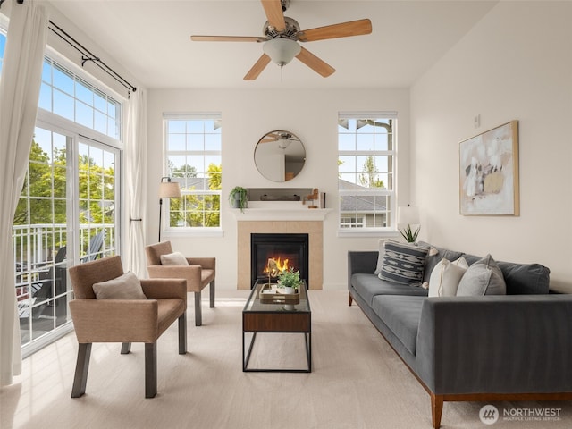 living room with a tiled fireplace, a ceiling fan, carpet floors, and a wealth of natural light