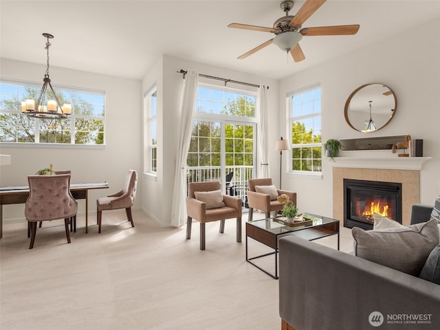 living room featuring baseboards, light carpet, ceiling fan with notable chandelier, and a tile fireplace