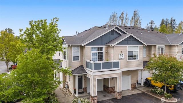 view of front facade featuring roof with shingles, an attached garage, driveway, and a balcony