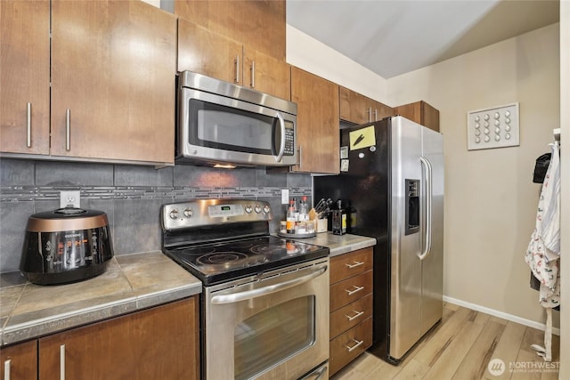 15720 Manor Way Unit C5, Lynnwood, WA 98087 - kitchen with stainless steel appliances, light wood finished floors, tasteful backsplash, brown cabinets, and tile countertops