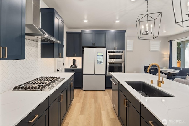 kitchen featuring decorative backsplash, light wood-type flooring, wall chimney exhaust hood, a sink, and appliances with stainless steel finishes