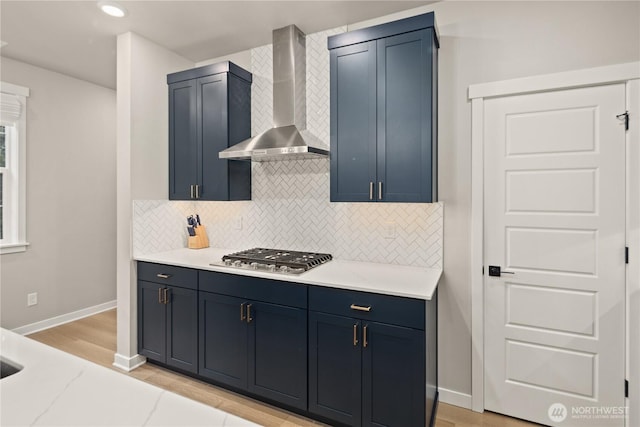 kitchen featuring stainless steel gas cooktop, baseboards, wall chimney exhaust hood, blue cabinets, and backsplash