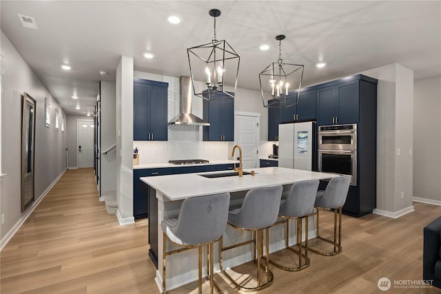 kitchen featuring wall chimney exhaust hood, gas stovetop, blue cabinets, tasteful backsplash, and a sink