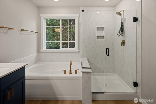 full bathroom featuring vanity, a marble finish shower, a garden tub, and wood finished floors