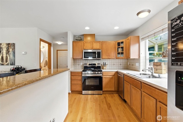 kitchen featuring decorative backsplash, glass insert cabinets, a sink, light wood-style flooring, and stainless steel appliances