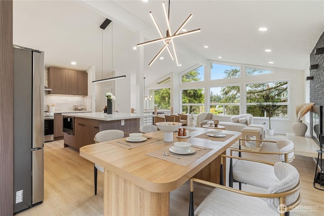 dining room featuring a fireplace, light wood-type flooring, beam ceiling, high vaulted ceiling, and recessed lighting