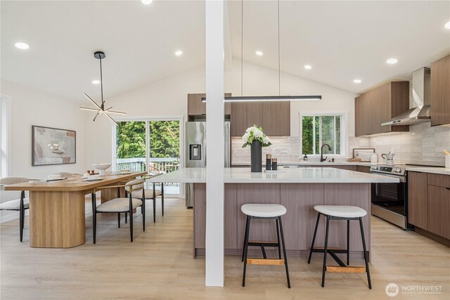 kitchen with a kitchen bar, modern cabinets, light countertops, stainless steel electric stove, and wall chimney exhaust hood