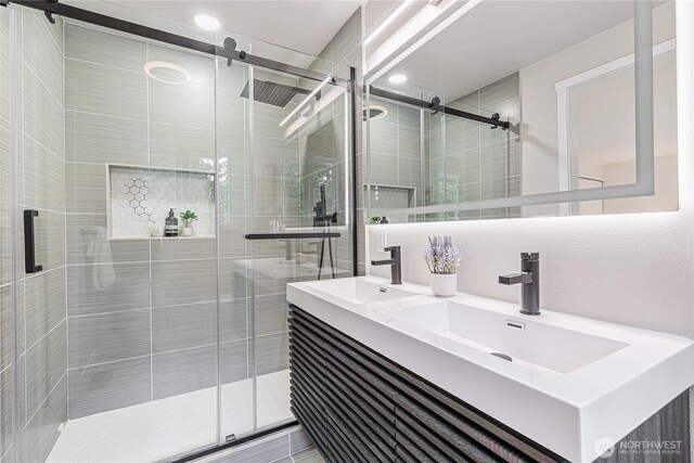 full bath featuring double vanity, a sink, and a shower stall