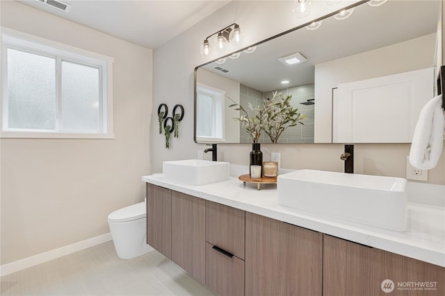 full bathroom featuring a sink, baseboards, a tile shower, and toilet