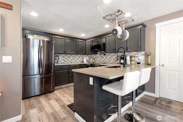 kitchen with light wood-type flooring, light countertops, a sink, freestanding refrigerator, and a peninsula