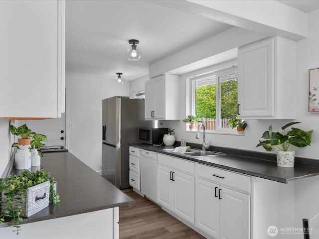 kitchen with dark countertops, a sink, light wood finished floors, stainless steel appliances, and white cabinetry