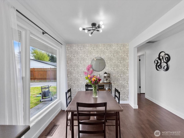 dining space with visible vents, dark wood-style flooring, an accent wall, baseboards, and a chandelier