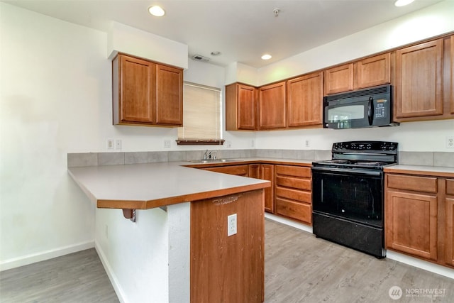 kitchen featuring visible vents, brown cabinets, black appliances, a peninsula, and light wood-style floors