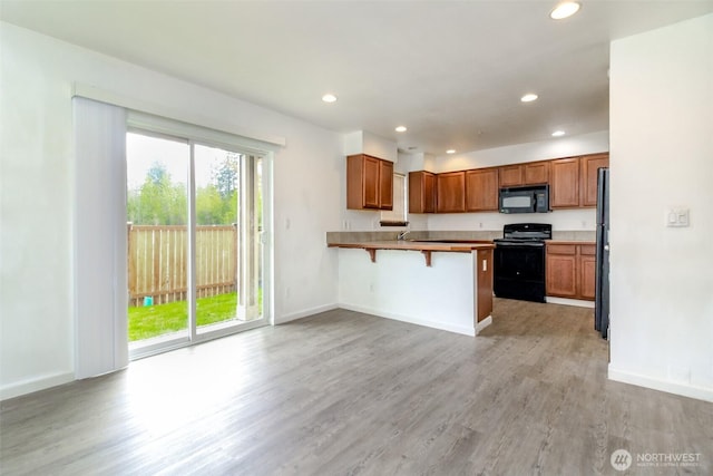 kitchen with a peninsula, light wood-style floors, a kitchen bar, recessed lighting, and black appliances
