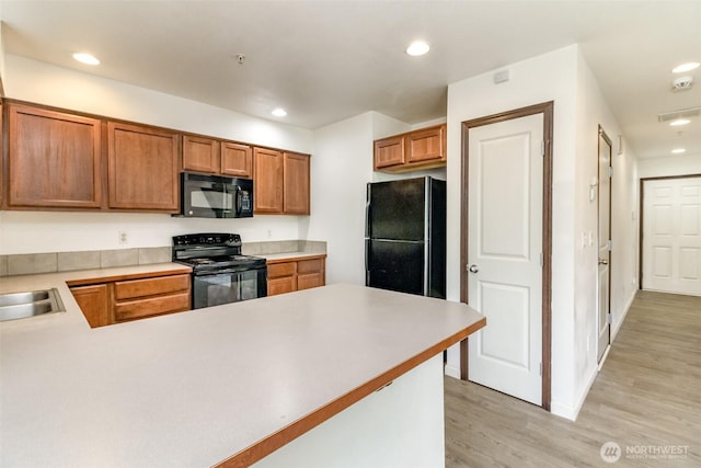 kitchen with a peninsula, recessed lighting, light countertops, light wood finished floors, and black appliances