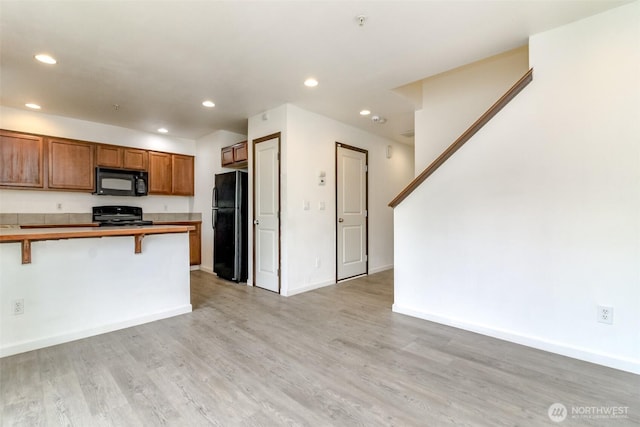 kitchen featuring brown cabinets, light wood finished floors, recessed lighting, a kitchen bar, and black appliances