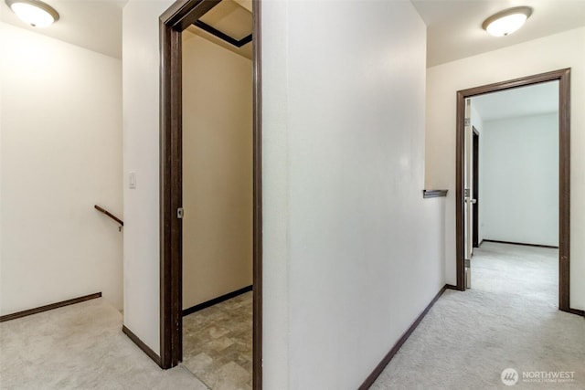 hall featuring baseboards, light carpet, and an upstairs landing