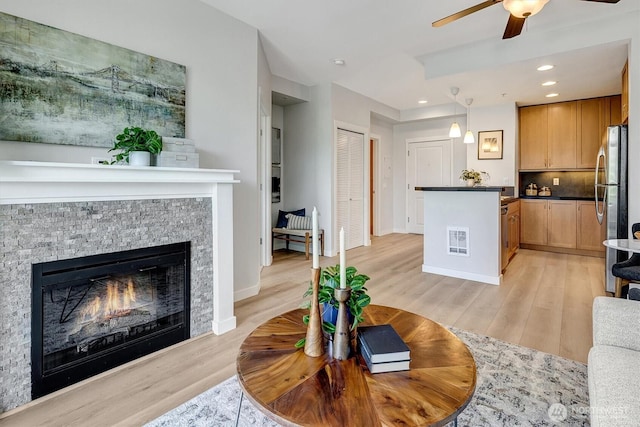 living area with a ceiling fan, visible vents, a stone fireplace, light wood-style floors, and recessed lighting
