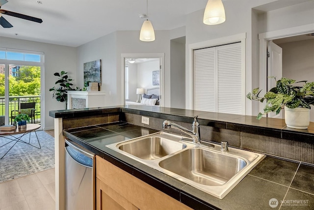 kitchen with a sink, dishwasher, ceiling fan, hanging light fixtures, and dark countertops