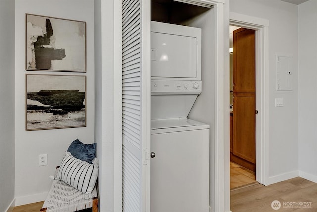 laundry room with laundry area, stacked washer / dryer, baseboards, and light wood-type flooring