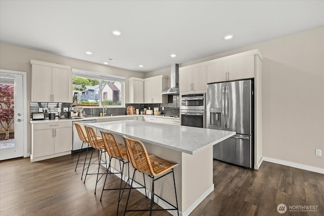 kitchen featuring a breakfast bar area, wall chimney exhaust hood, tasteful backsplash, dark wood finished floors, and stainless steel appliances