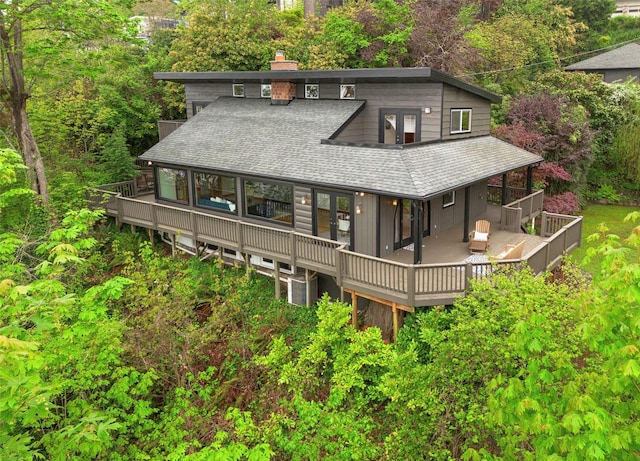 rear view of house with french doors, a deck, a chimney, and roof with shingles
