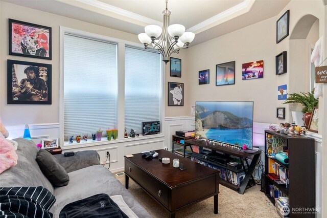 living room with wainscoting, an inviting chandelier, ornamental molding, a decorative wall, and carpet flooring