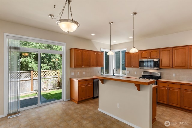 4504 5th Ave NW, Olympia, WA 98502 - kitchen featuring stainless steel microwave, gas range, backsplash, brown cabinetry, and light countertops