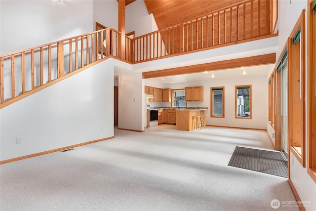 unfurnished living room with baseboards, light carpet, high vaulted ceiling, and visible vents