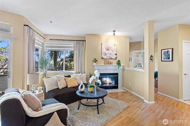 living room with a tiled fireplace, baseboards, and light wood-type flooring