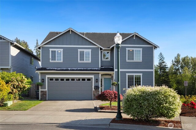 view of front facade featuring board and batten siding, an attached garage, driveway, stone siding, and fence