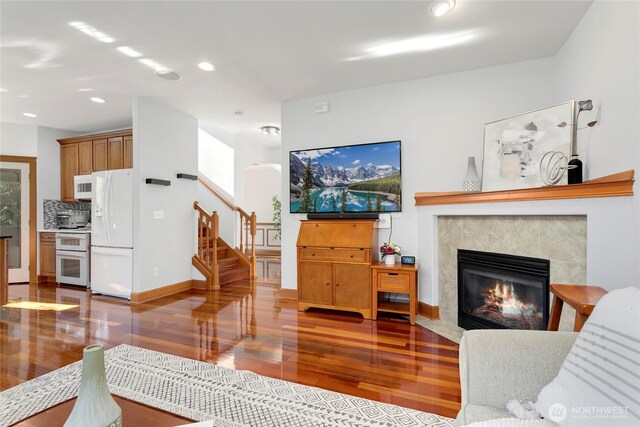 living room featuring wood finished floors, stairway, recessed lighting, a tile fireplace, and baseboards