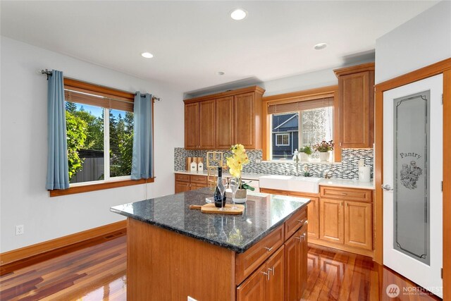 kitchen with a sink, tasteful backsplash, dark wood-type flooring, a kitchen island, and brown cabinets