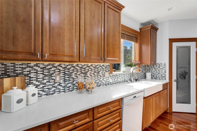 kitchen featuring white dishwasher, a sink, light countertops, and tasteful backsplash
