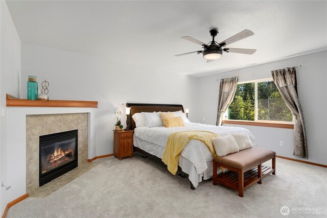 carpeted bedroom featuring a tiled fireplace, ceiling fan, and baseboards