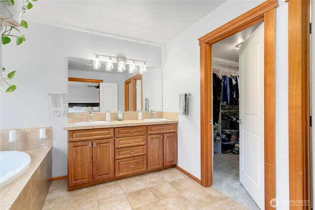 bathroom with a garden tub, double vanity, a spacious closet, and baseboards