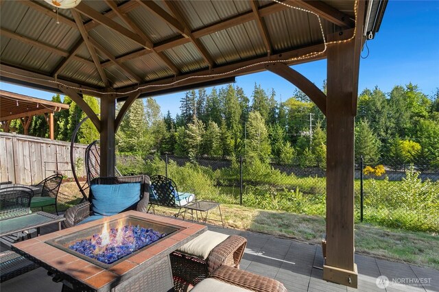 view of patio featuring an outdoor fire pit, fence, a forest view, and a gazebo