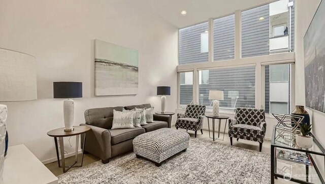 living room featuring baseboards, plenty of natural light, recessed lighting, and a high ceiling