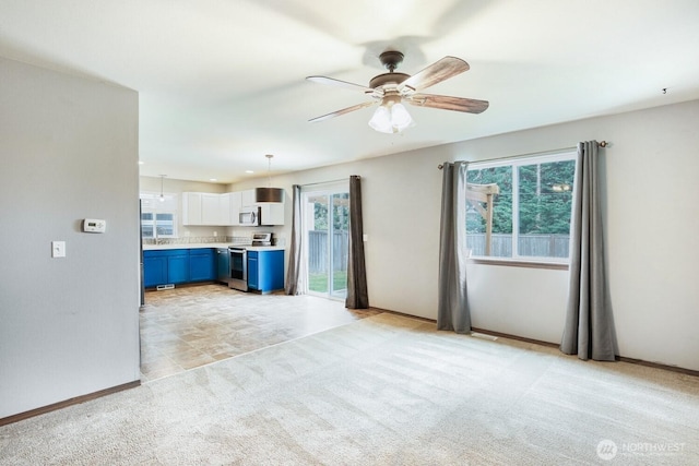 unfurnished living room featuring a ceiling fan, baseboards, light colored carpet, and a sink