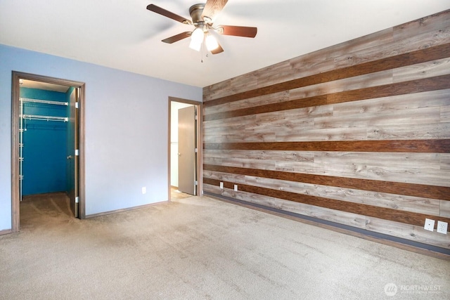 unfurnished bedroom featuring carpet flooring, a walk in closet, wood walls, a ceiling fan, and a closet