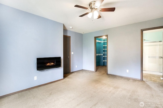 interior space featuring carpet floors, baseboards, a warm lit fireplace, a spacious closet, and ensuite bath