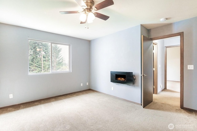 unfurnished living room with baseboards, a ceiling fan, carpet, and a lit fireplace