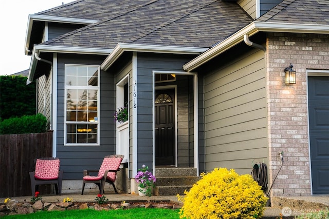 doorway to property with a garage, a shingled roof, and fence
