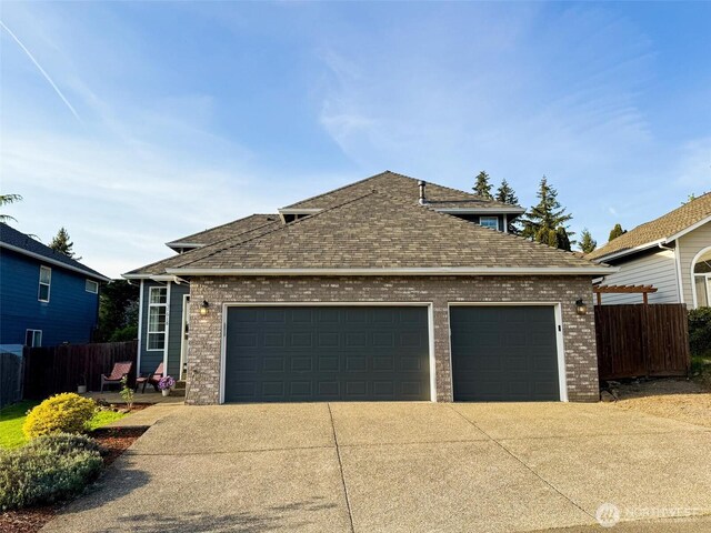 view of front of house featuring fence, roof with shingles, brick siding, an attached garage, and driveway