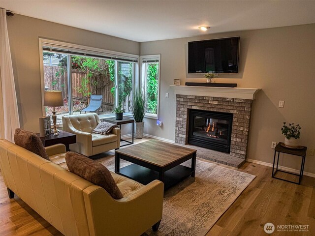 living area featuring baseboards, a brick fireplace, and wood finished floors