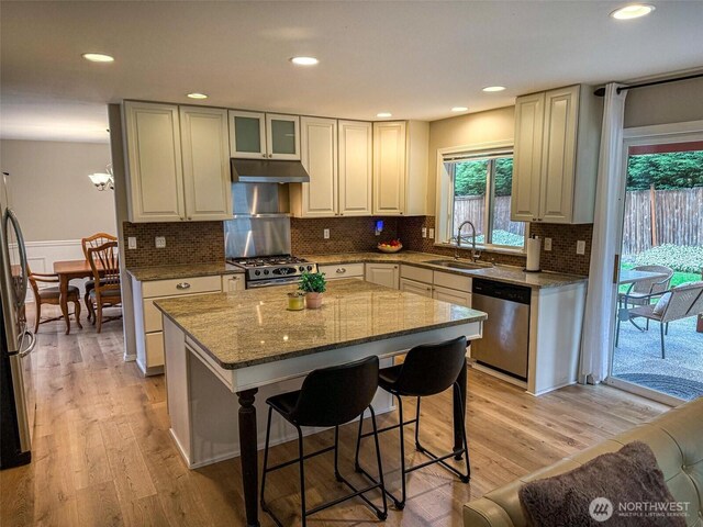 kitchen featuring a kitchen breakfast bar, under cabinet range hood, a sink, dark stone countertops, and stainless steel appliances