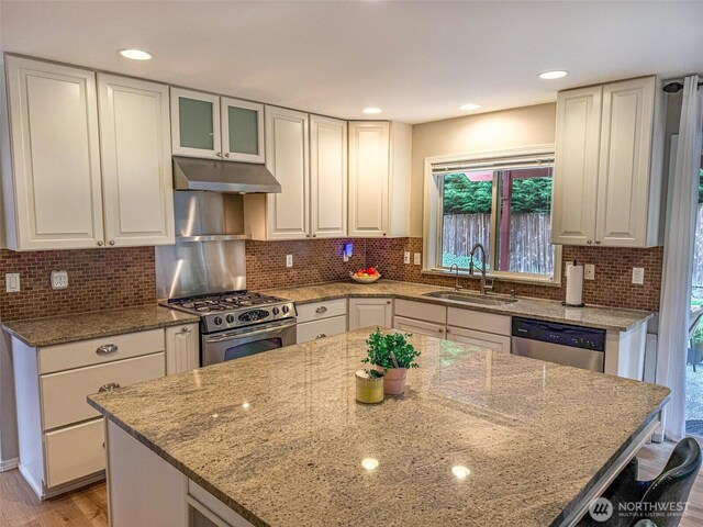 kitchen featuring light stone counters, a sink, appliances with stainless steel finishes, and under cabinet range hood