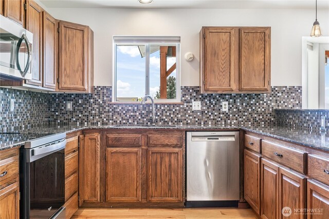 5208 Tumac Dr, Yakima, WA 98901 - kitchen featuring appliances with stainless steel finishes, brown cabinets, a sink, dark stone counters, and light wood-style flooring